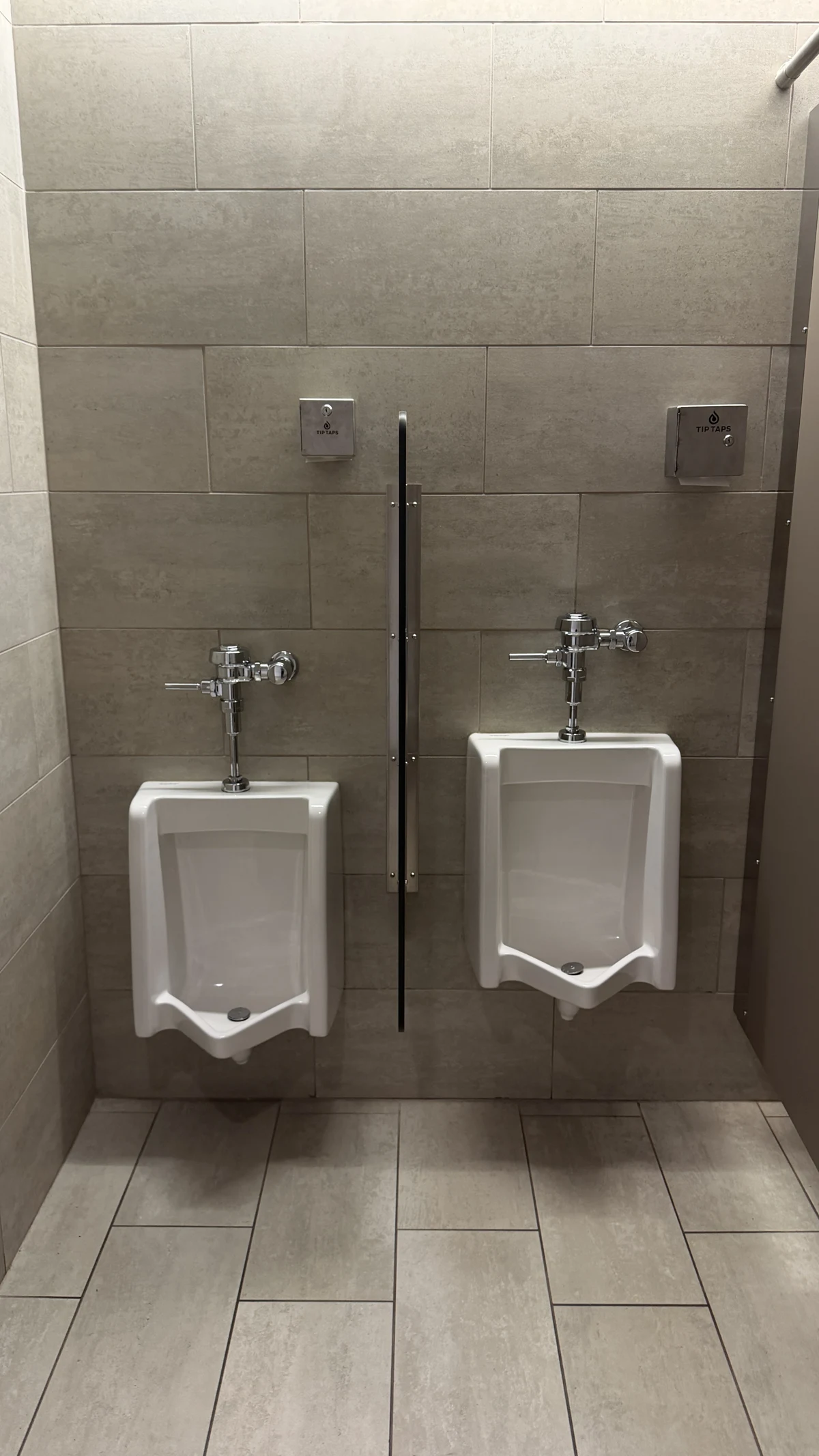 Two stainless-steel Tip Taps dispensers mounted beside urinals