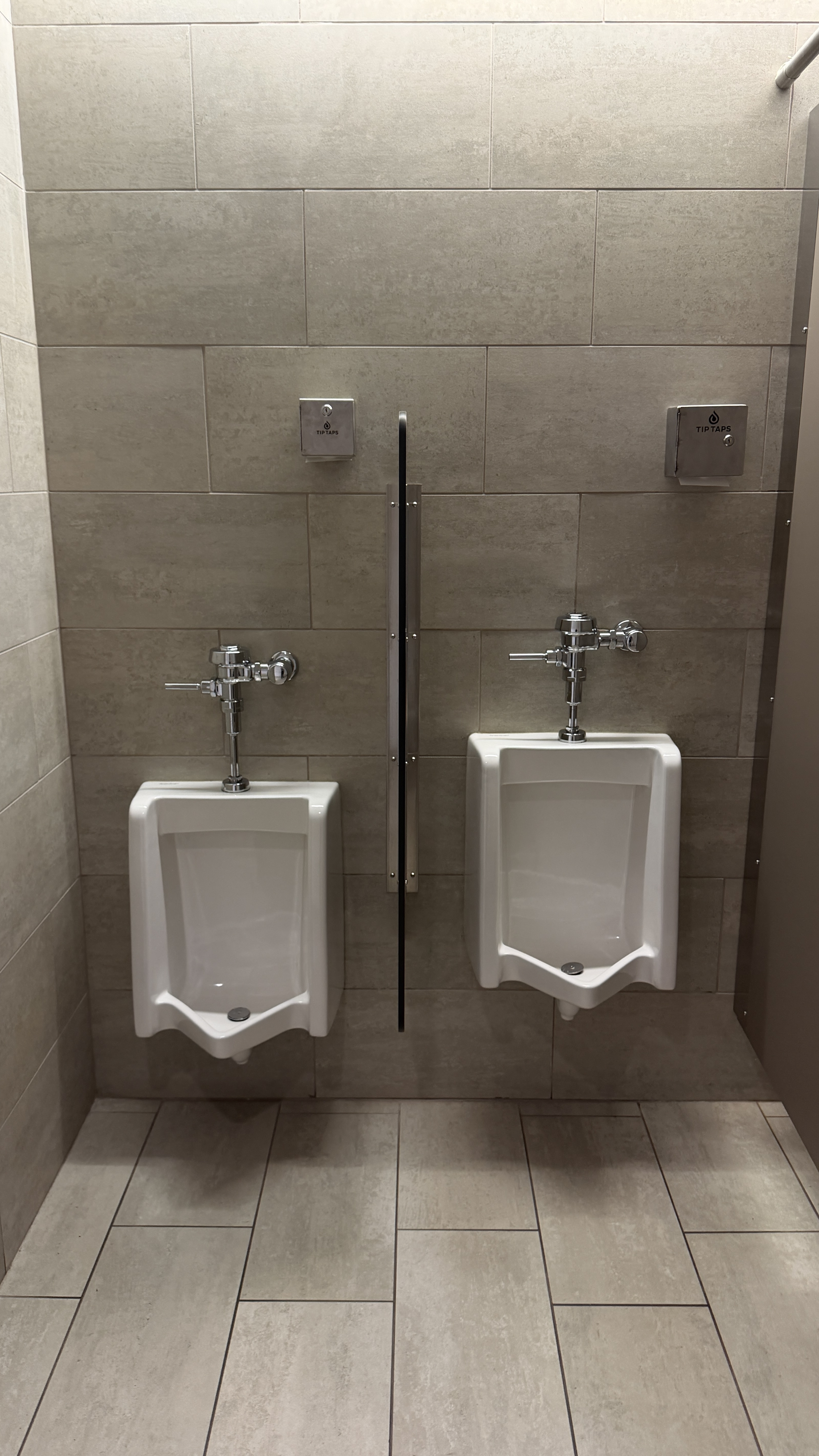 Tip Taps dispensers installed next to public urinals in a commercial restroom